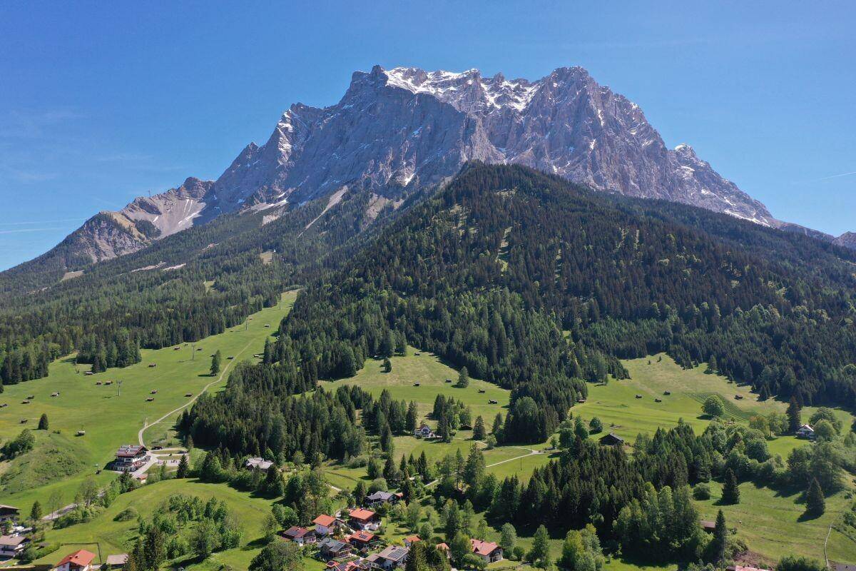 Weitläufige alpine Landschaft mit bewaldeten Hängen, grünen Tälern und schneebedeckten Gipfeln.