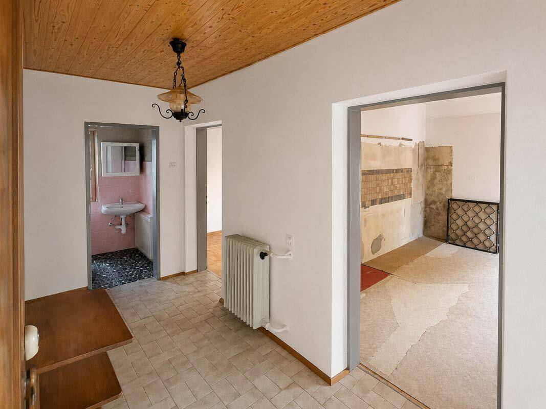 Flur mit Fliesenboden, der zu einem Badezimmer und einer Küche führt, mit Holzdecke.
