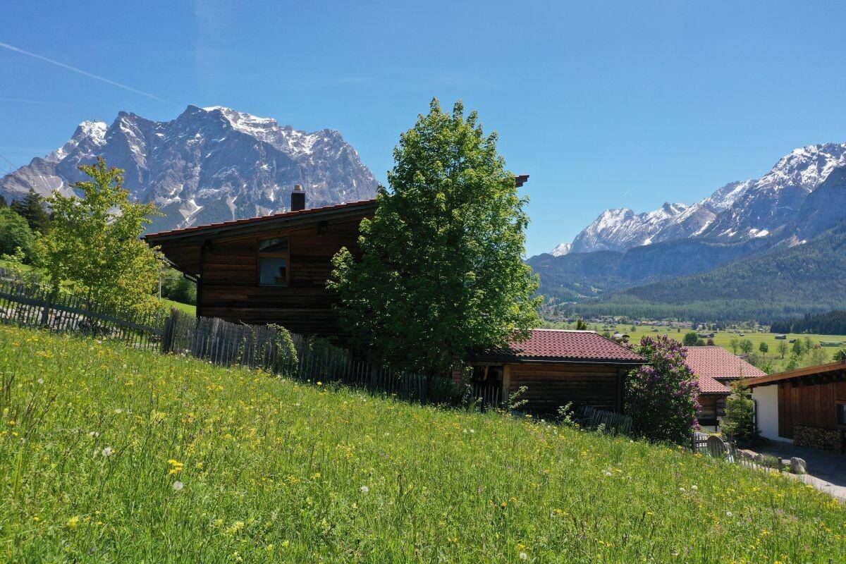Rustikales Holzhaus auf einem sonnigen Hügel mit weitem Blick auf die majestätischen Berge.