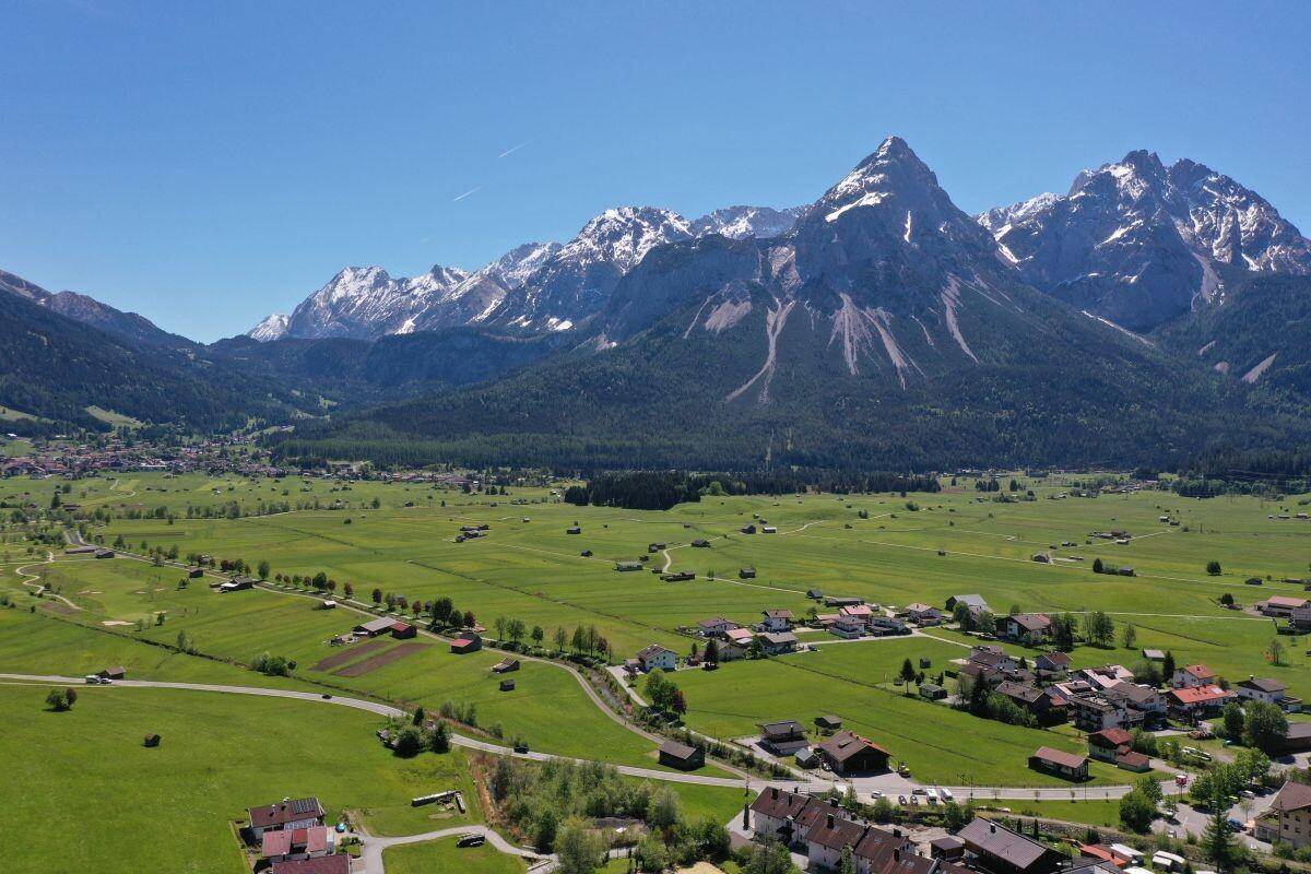Luftaufnahme eines malerischen Dorfes eingebettet in eine weite grüne Landschaft mit hohen Bergen.
