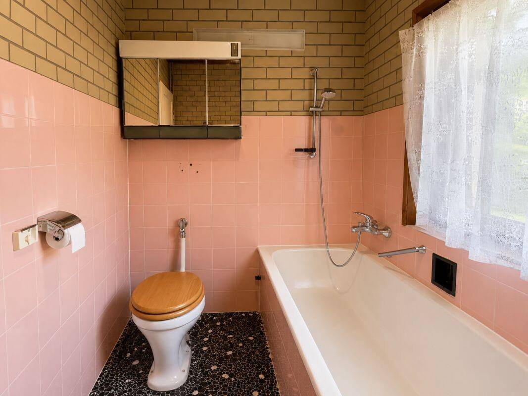 Badezimmer im Stil der 80er Jahre mit rosa Fliesen, Badewanne und Fenster.
