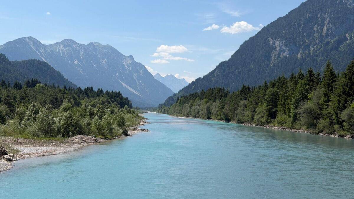 Weites Flusstal mit türkisfarbenem Wasser, umgeben von dichten Wäldern und hohen Bergen.