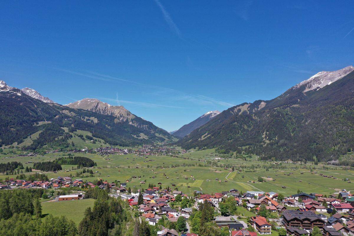 Beeindruckende Luftaufnahme eines alpinen Tals mit Siedlungen, Wäldern und hohen Bergen.