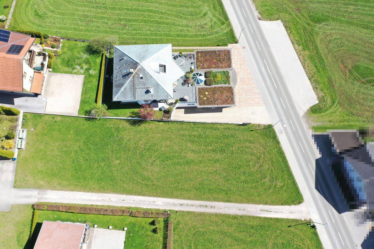 Luftaufnahme eines Wohnhauses mit gepflegtem Garten, Zufahrt und angrenzenden Grünflächen.