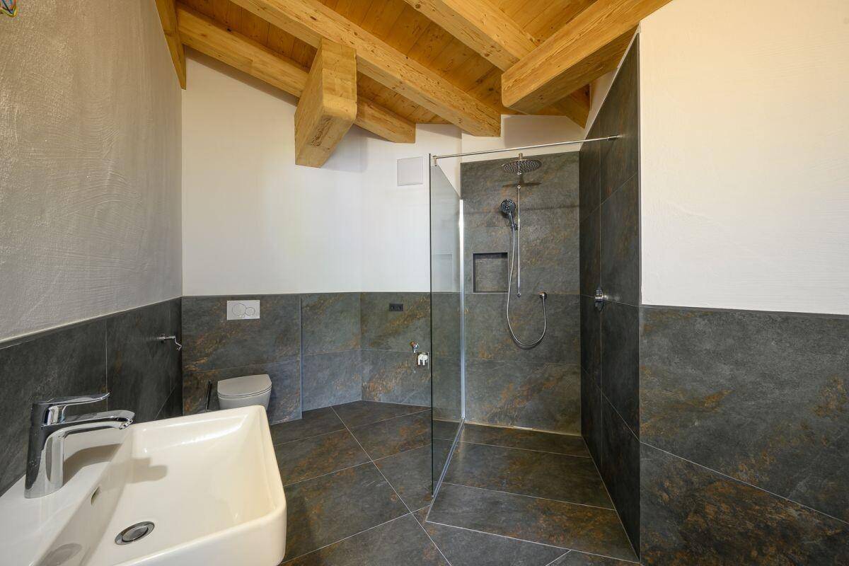 Modernes Badezimmer mit dunklen Fliesen, begehbarer Dusche und Holzbalkendecke.