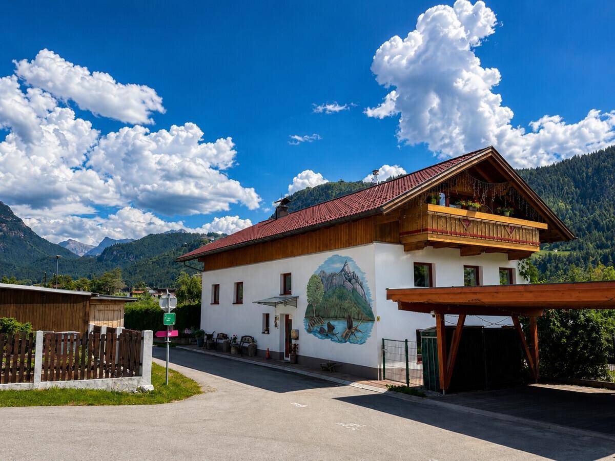 Charmantes Haus mit traditioneller Fassadenmalerei, Holzbalkon und Bergblick unter blauem Himmel.