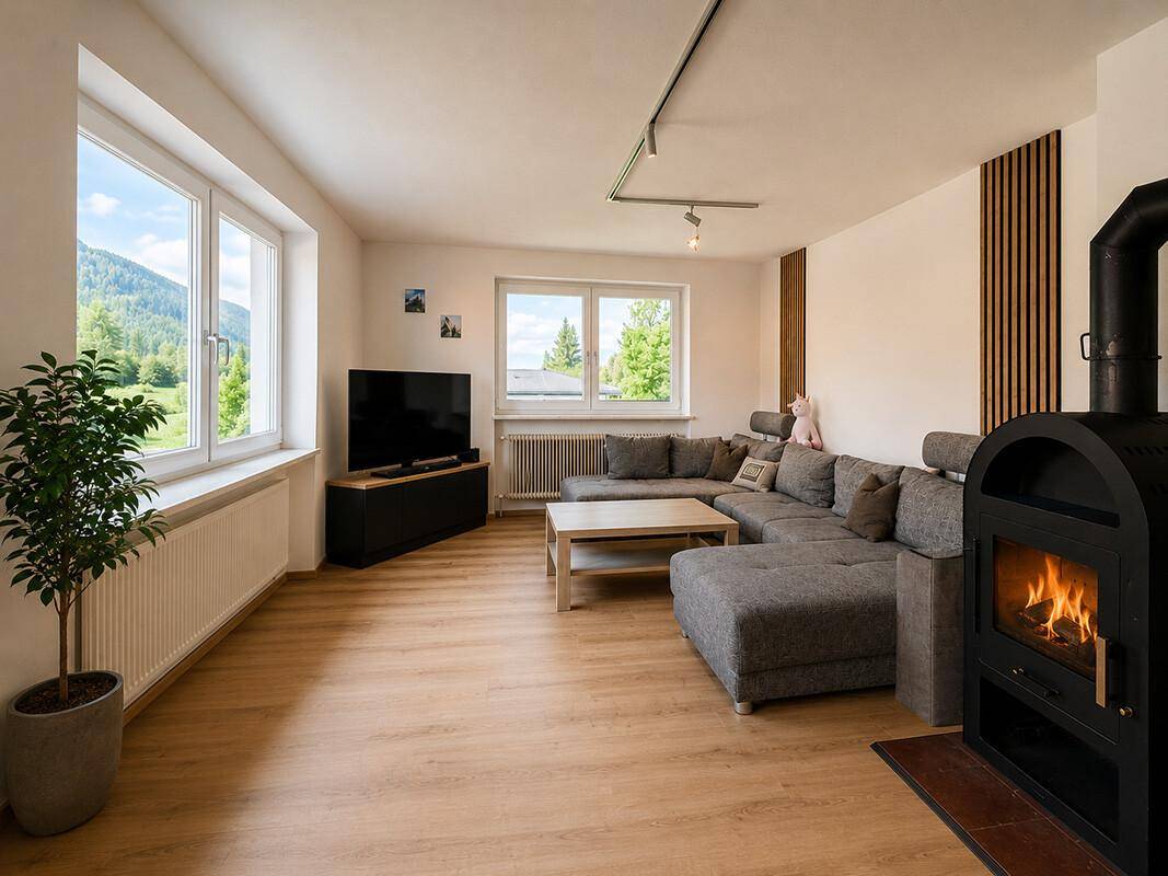 Helles Wohnzimmer mit Kaminofen, großem Sofa und Holzboden mit Bergblick.
