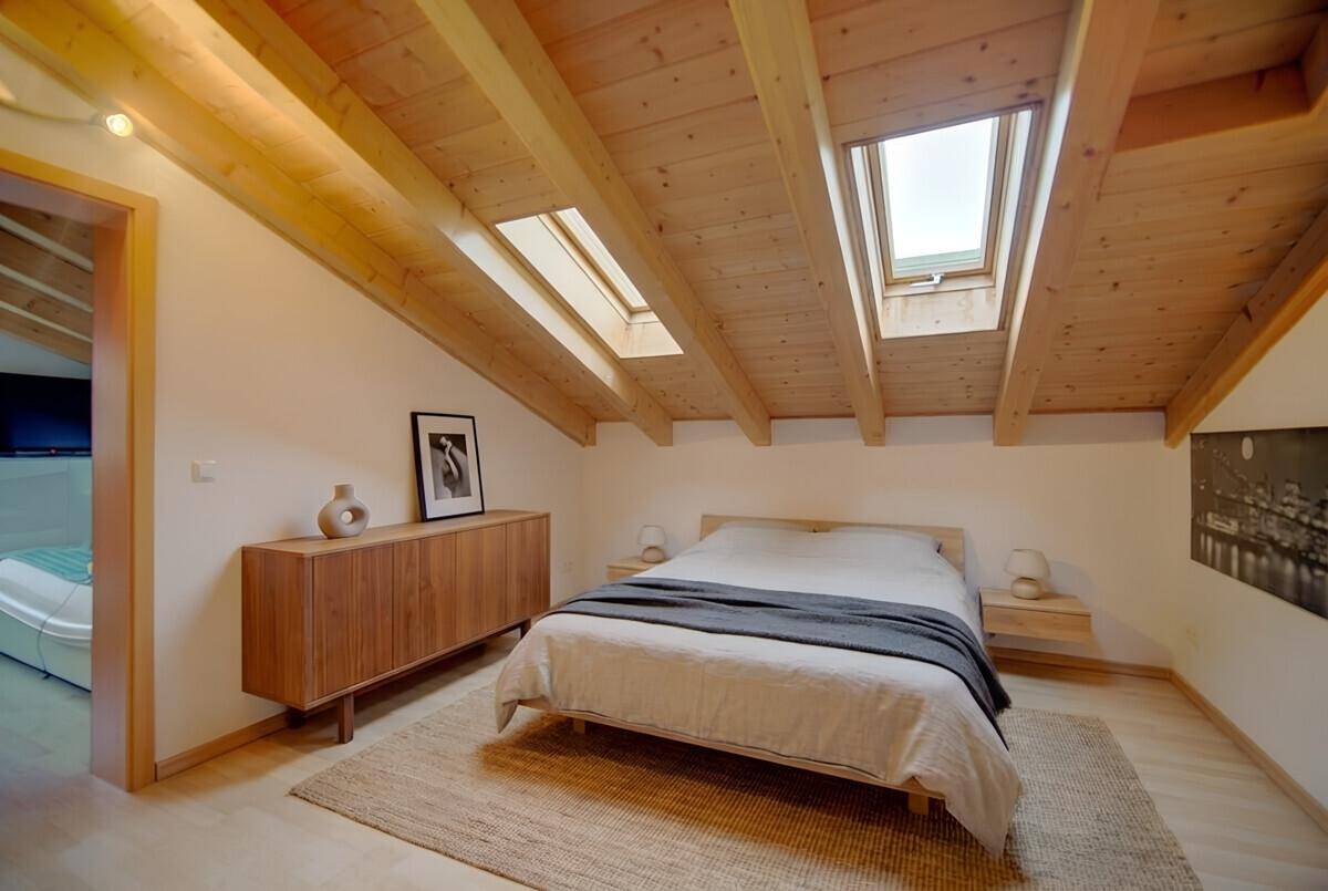 Helles Schlafzimmer im Dachgeschoss mit Holzbalken, Dachfenstern und Holzboden.