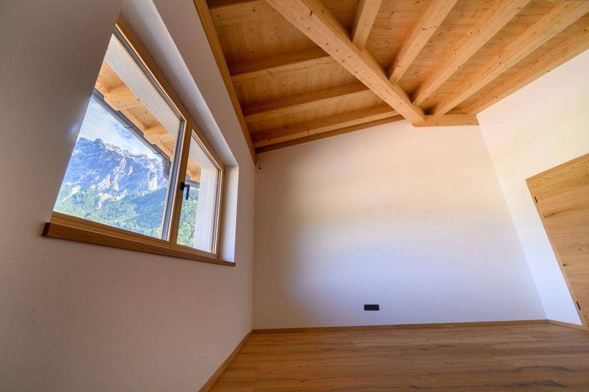 Helles Zimmer mit Holzbalkendecke und Fenster, das einen weiten Blick auf die Berge bietet.