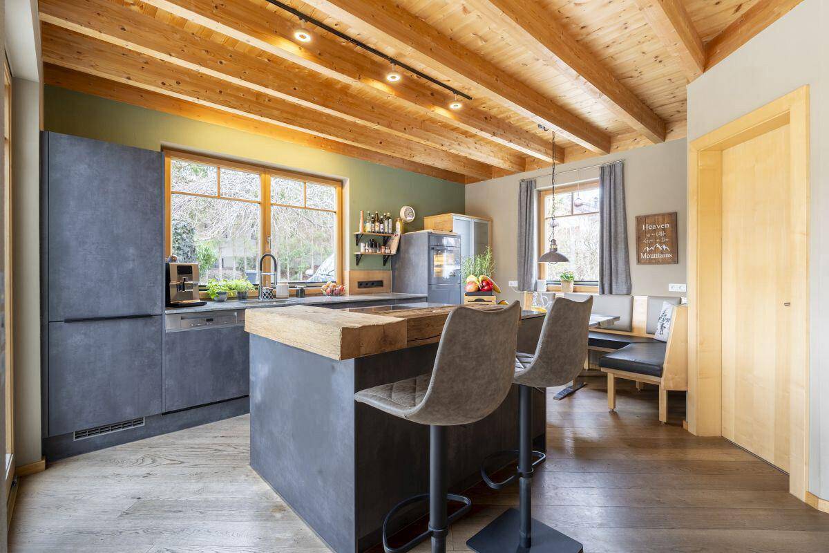 Moderne Küche mit dunklen Fronten, Holztheke und integriertem Essbereich am Fenster.