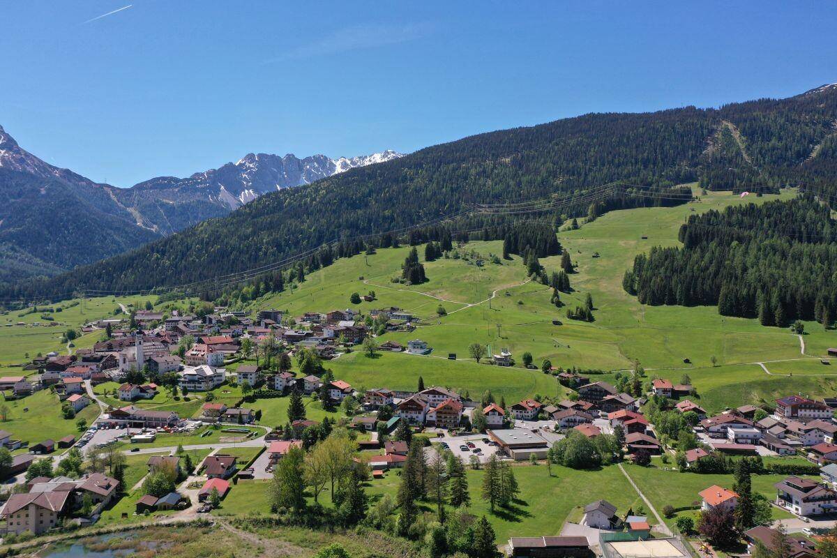 Luftaufnahme eines charmanten Dorfes umgeben von grünen Wäldern und sanften Berghängen.