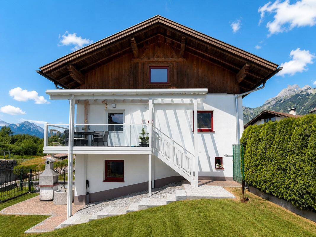 Rückseite des Hauses mit Balkon, Außentreppe und gepflegtem Gartenbereich mit Grill.
