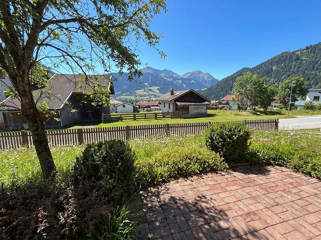 Gepflasterter Weg im Vorgarten mit Blick auf die umliegende grüne Landschaft und Berge.