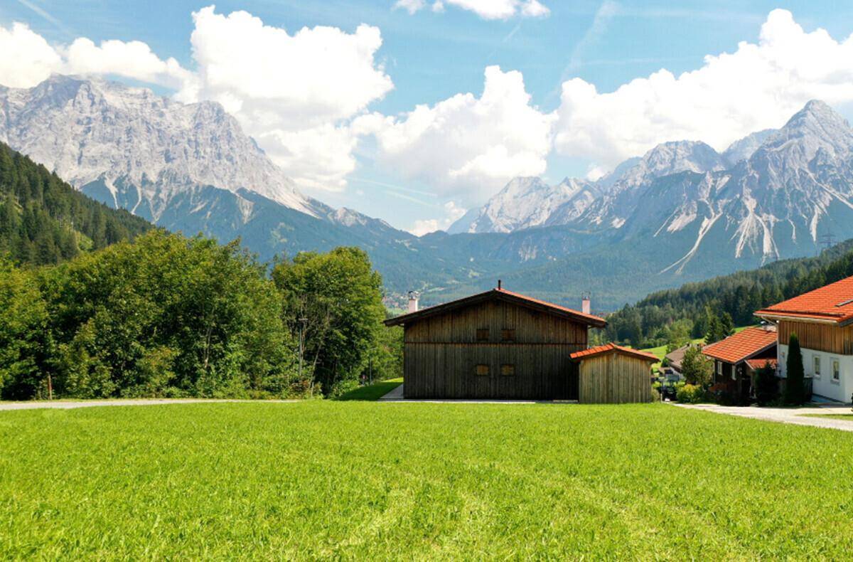 Traditionelles Holzhaus mit rotem Dach und weitem Blick auf grüne Wiesen und die Alpen.