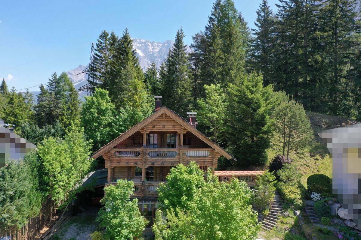 Charmantes Holzhaus in den Bergen, umgeben von hohen Bäumen und mit Blick auf schneebedeckte Gipfel.