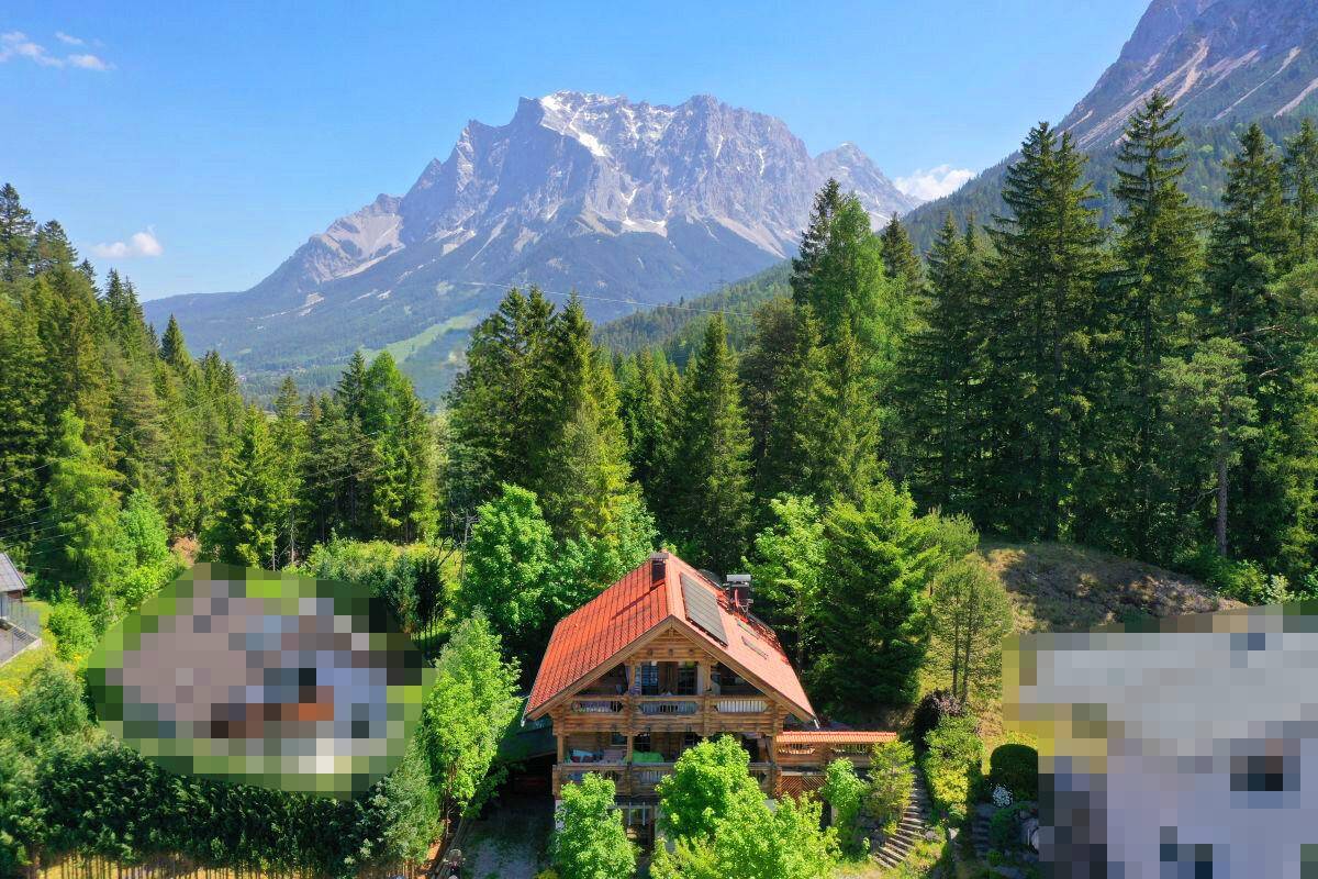 Malerisches Holzhaus vor der Kulisse majestätischer Berge und grüner Wälder unter blauem Himmel.