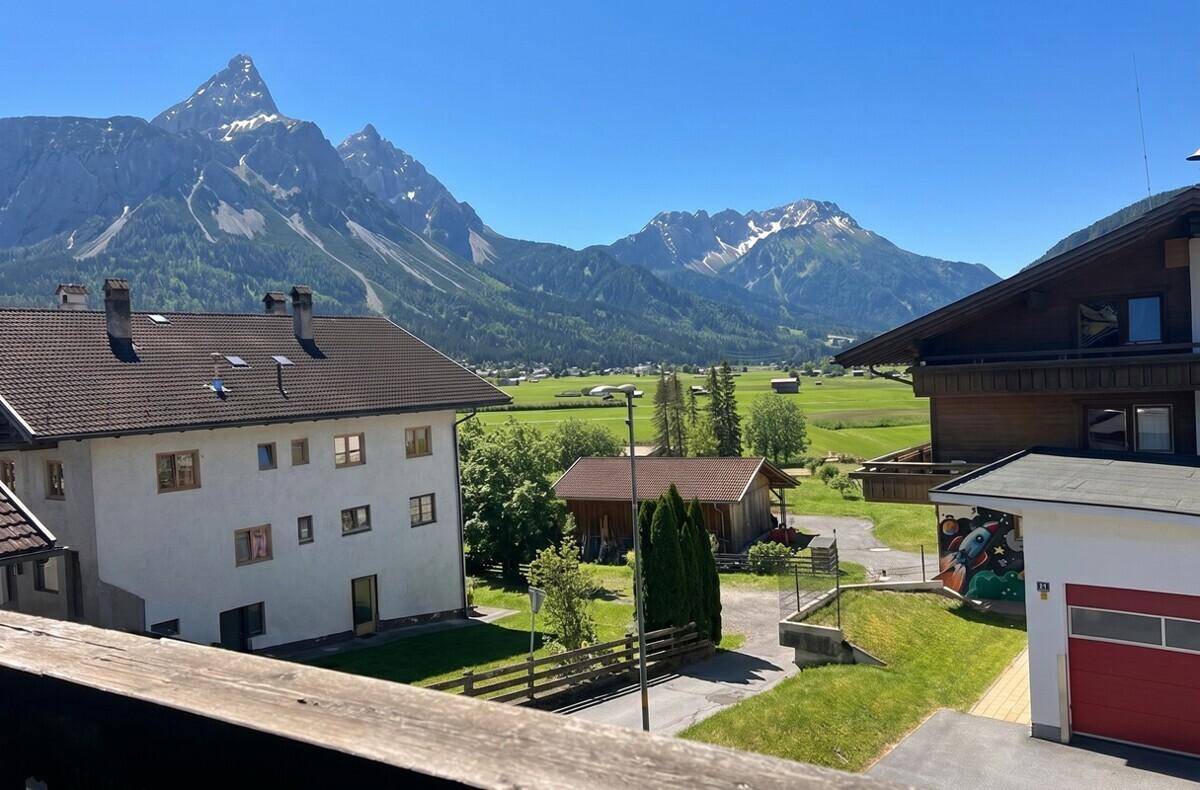 Panoramablick auf eine malerische Alpenlandschaft mit Häusern, grünen Wiesen und majestätischen Berggipfeln.