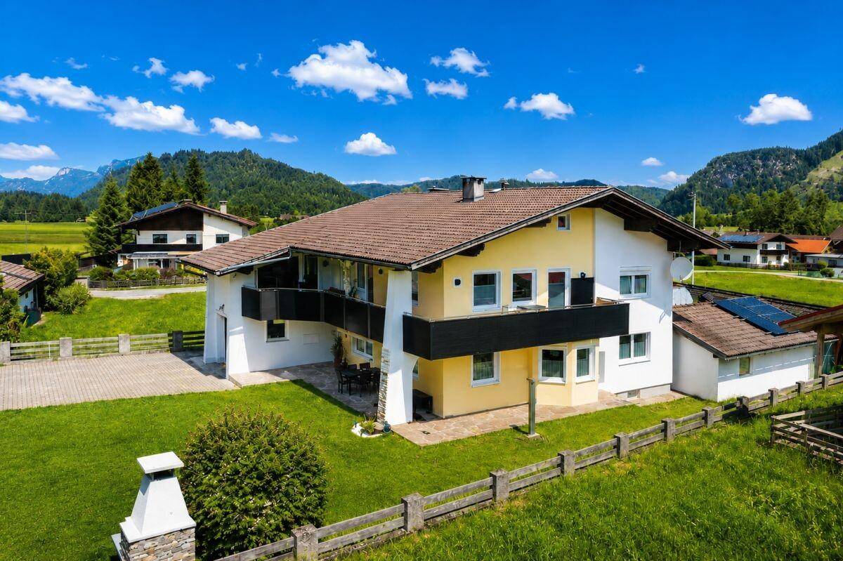 Großzügiges Einfamilienhaus mit gepflegtem Garten und Bergblick unter blauem Himmel.