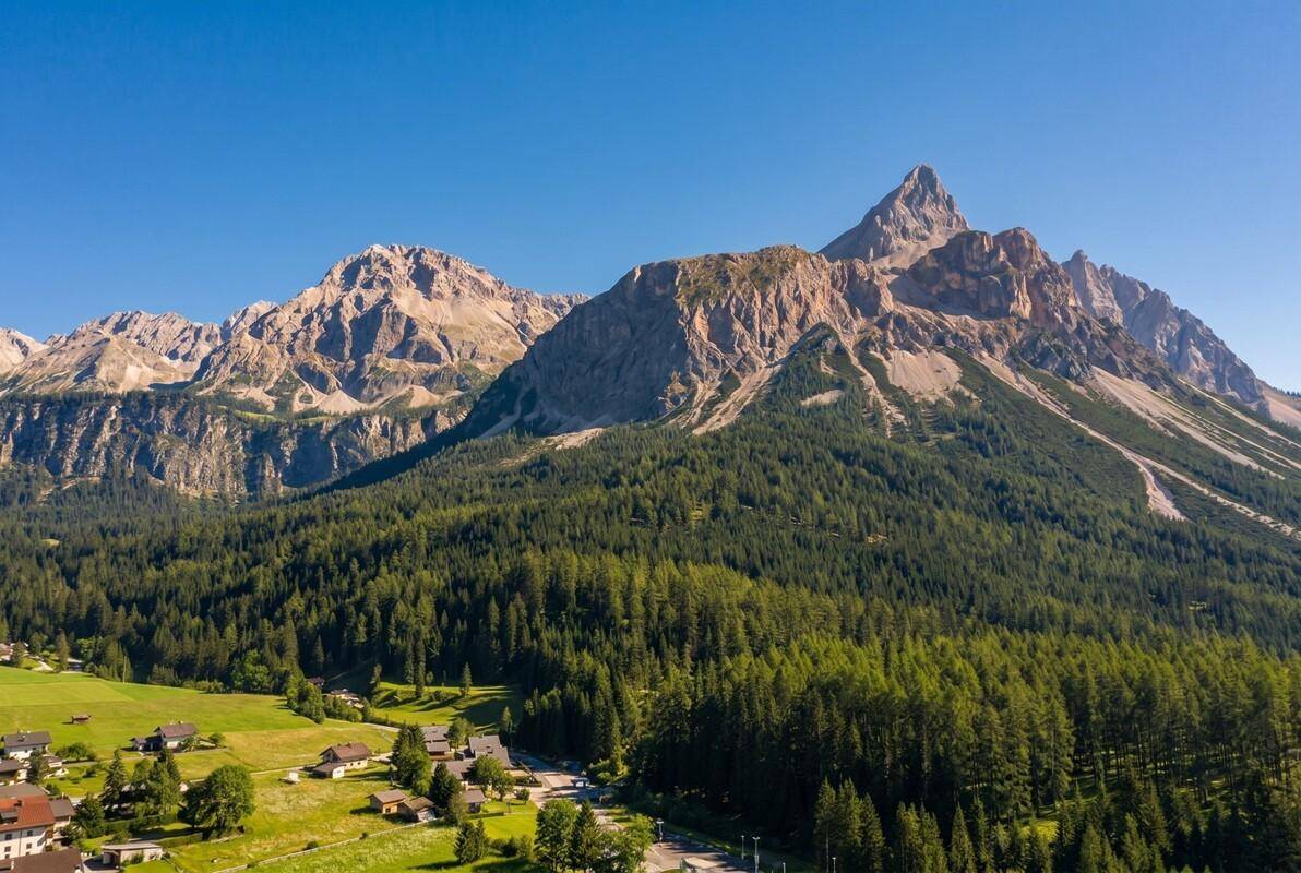 Majestätische Berglandschaft mit dichten Wäldern und vereinzelten Häusern im Vordergrund.