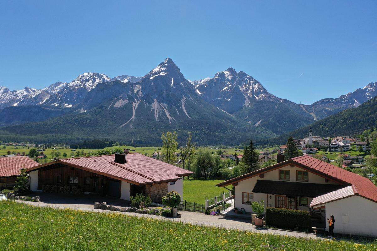 Zwei charmante Häuser mit roten Dächern und gepflegtem Garten vor einer atemberaubenden Berglandschaft.