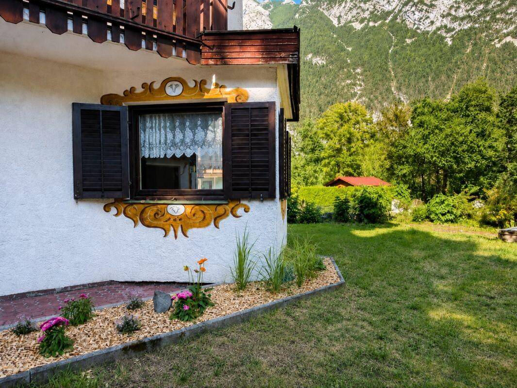 Detailansicht der Hausfassade mit traditioneller Malerei und einem kleinen Blumenbeet im Garten.