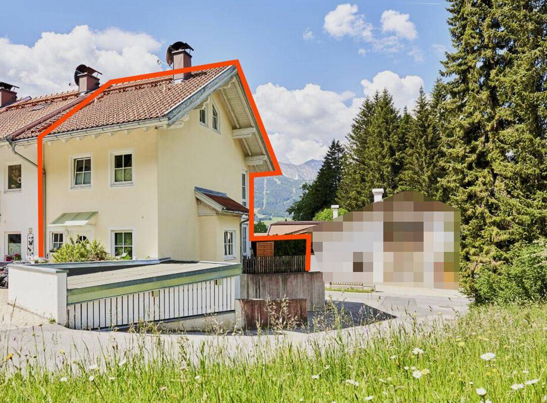 Seitenansicht des Hauses mit traditionellem Satteldach und Bergblick im Hintergrund unter blauem Himmel.