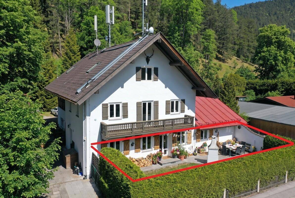 Alpines Einfamilienhaus mit Garten und Terrasse, umgeben von Natur, mit markierter Grundstücksgrenze.