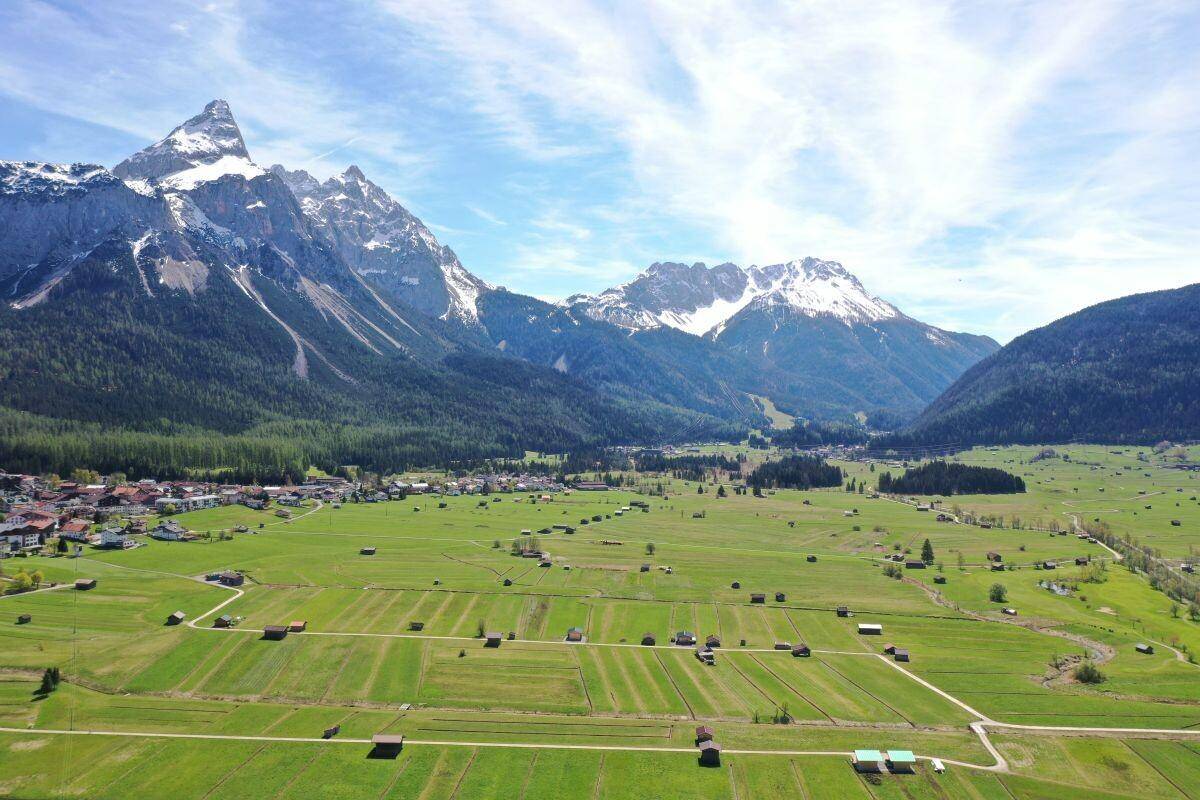 Weitläufige Luftaufnahme eines Tals mit einem Dorf, vielen kleinen Hütten und schneebedeckten Bergen im Hintergrund.