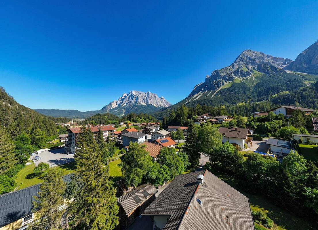 Weitläufige Luftaufnahme eines malerischen Dorfes in einem Tal, umgeben von Bergen und Wäldern.