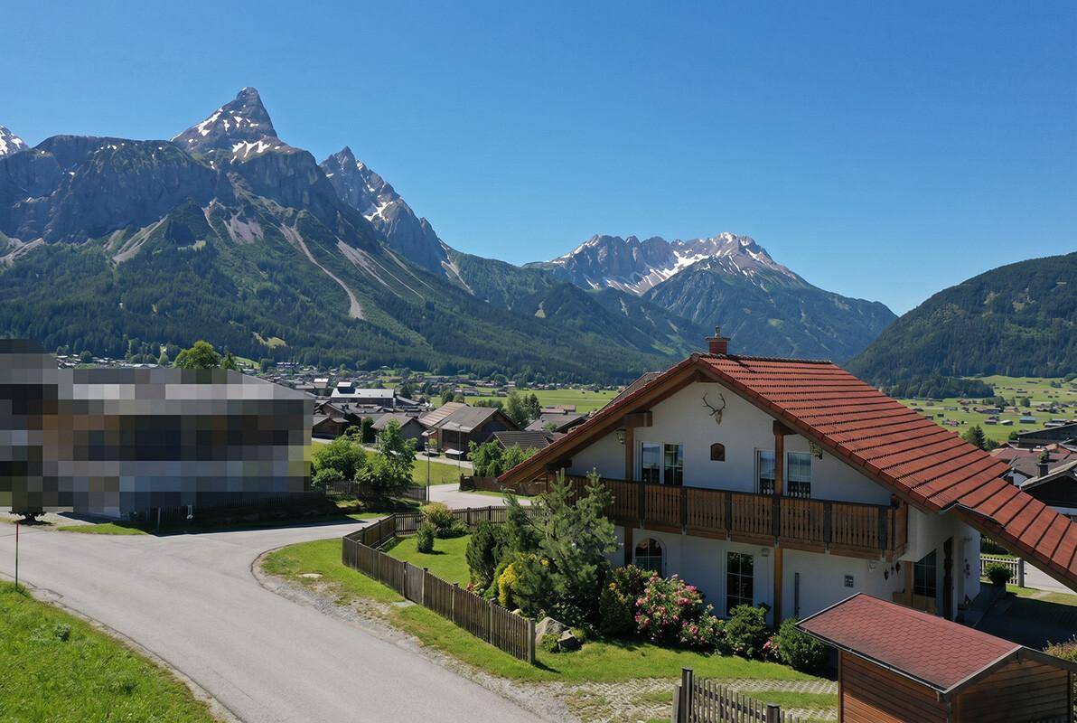 Traditionelles Haus mit Balkon und Satteldach, umgeben von alpiner Natur und Bergen.