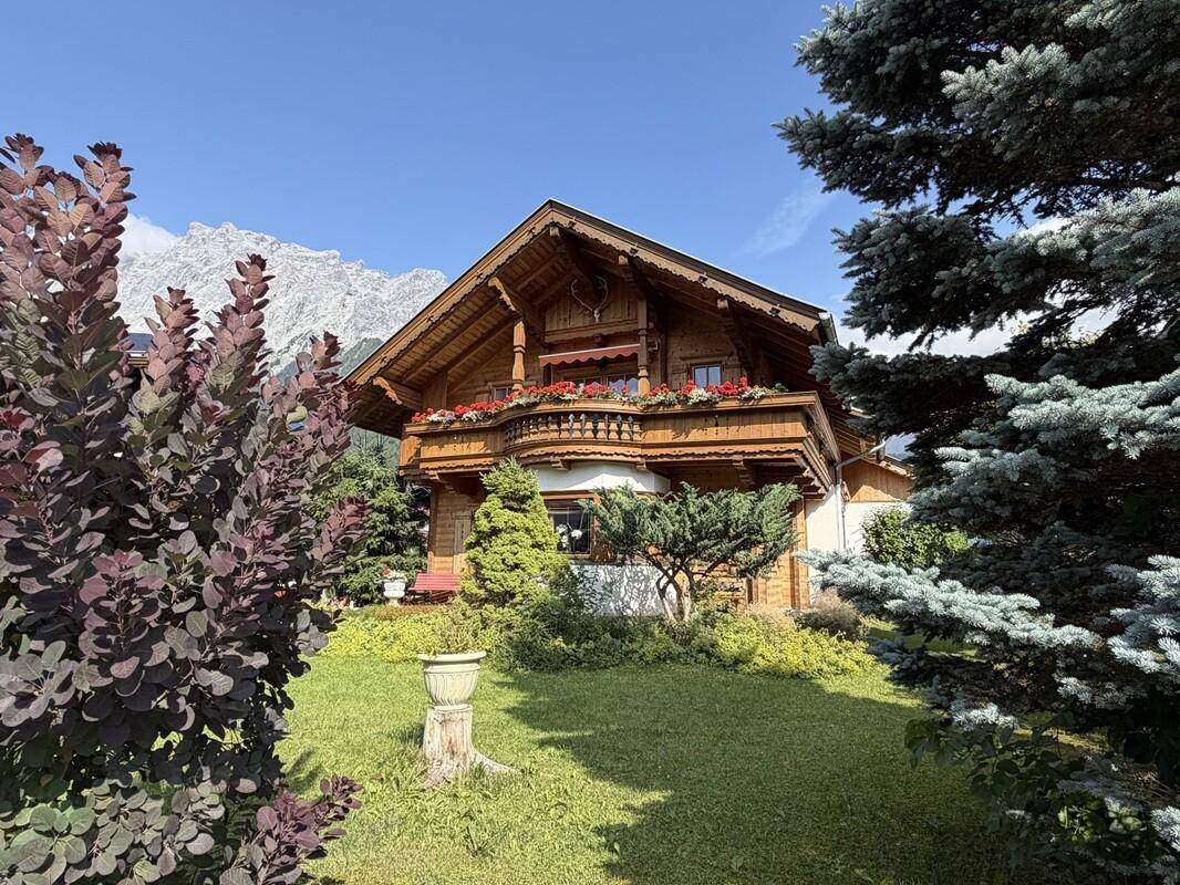 Detailansicht des Holzchalets mit gepflegtem Vorgarten und imposanter Bergkulisse.