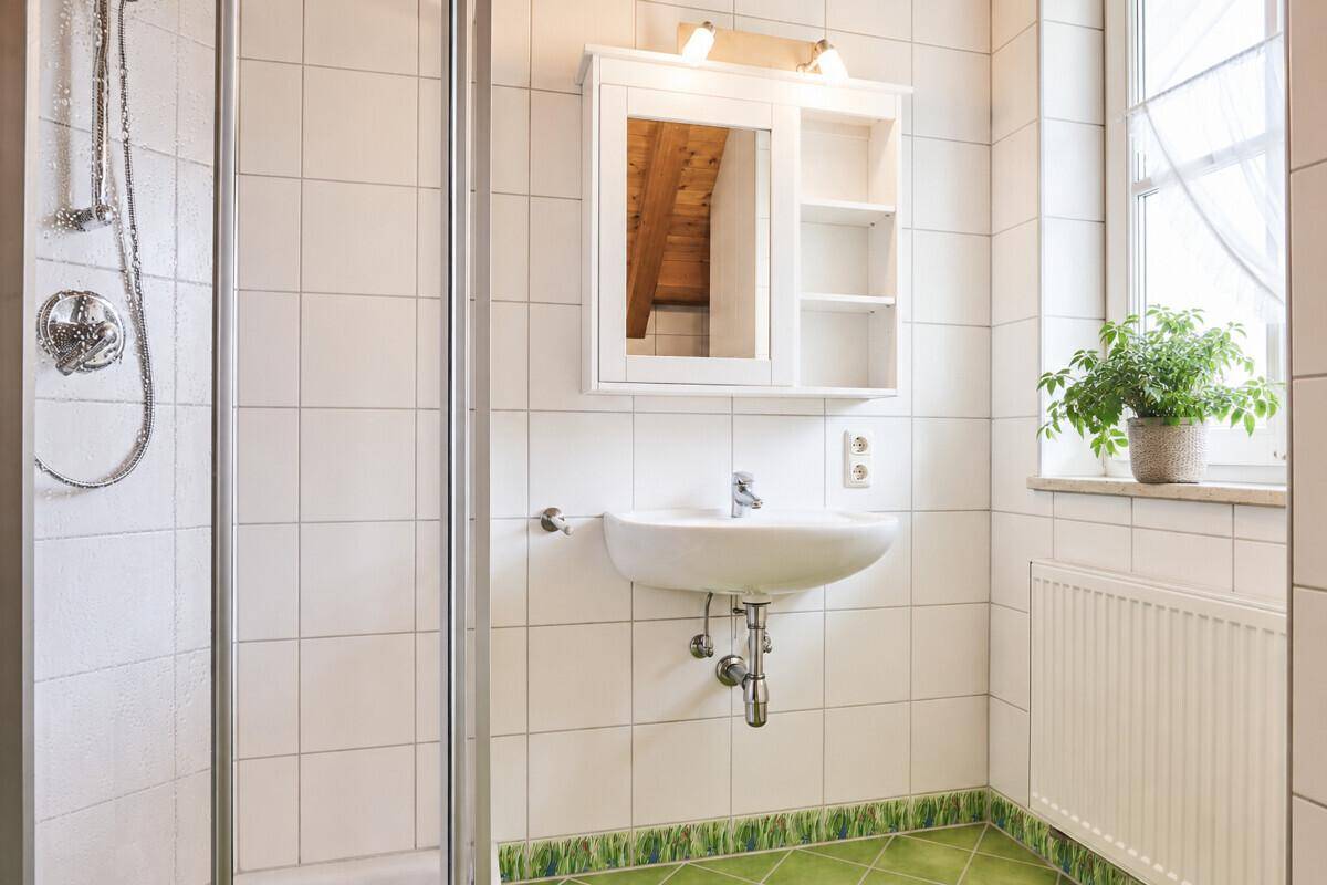 Badezimmer mit Duschkabine, Waschbecken, Spiegelschrank und Fenster, hell gefliest.