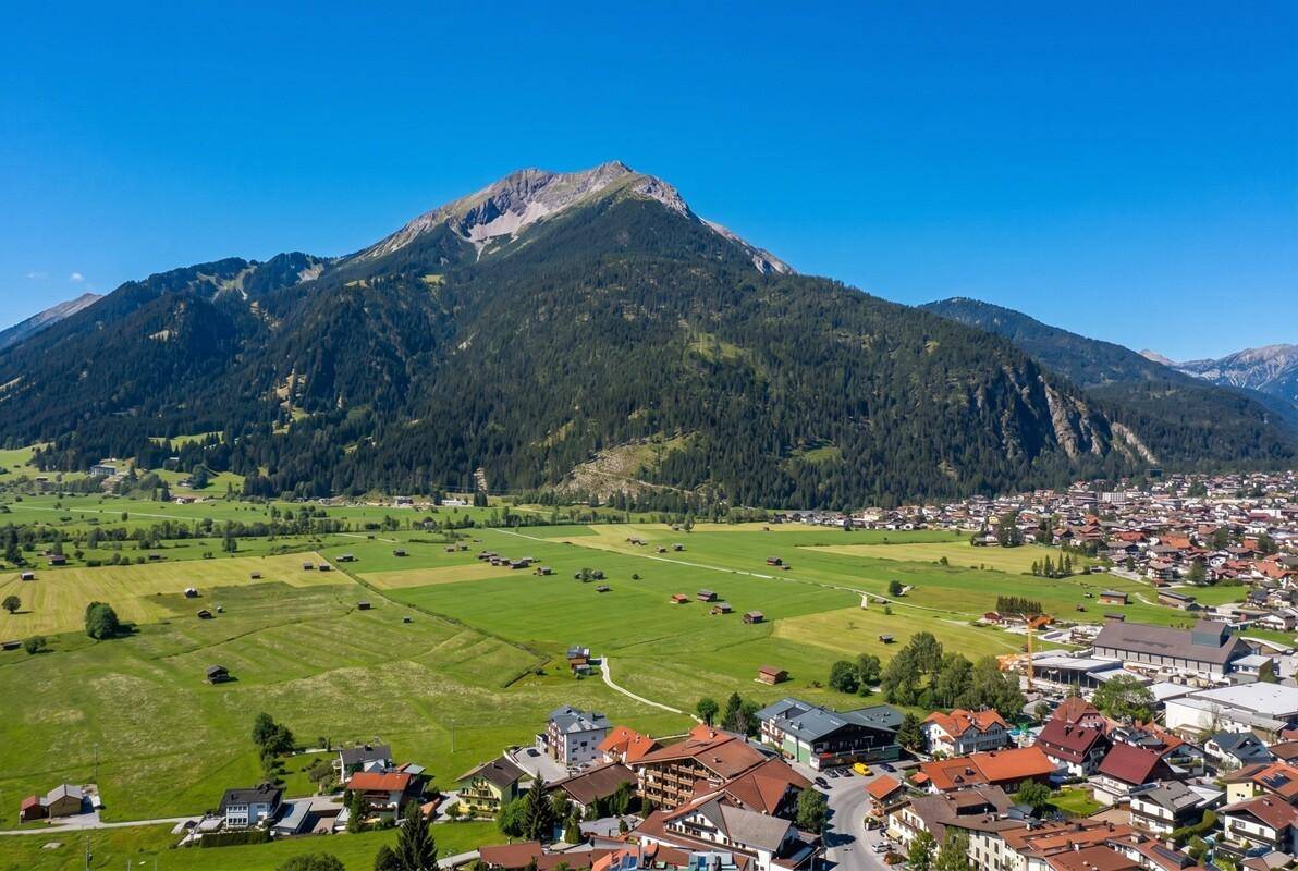 Panoramablick auf eine Stadt am Fuße eines Berges, umgeben von grünen Feldern und Wäldern.