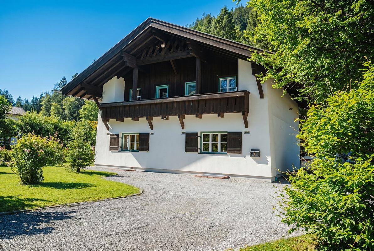Seitenansicht des traditionellen Hauses mit Holzbalkon und gepflegter Zufahrt im Grünen.