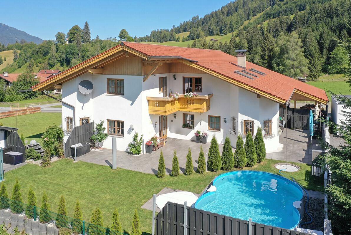 Rückansicht des Hauses mit gepflegtem Garten, Swimmingpool und Bergblick.