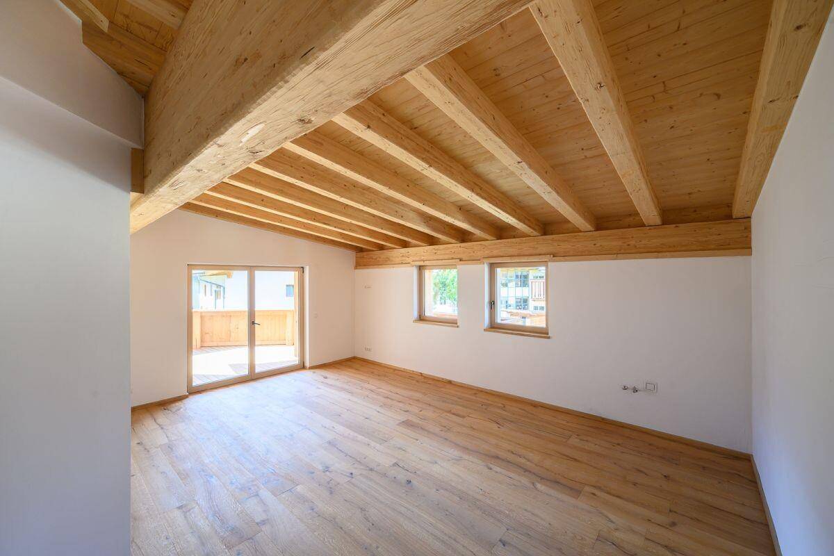 Geräumiger, heller Wohnbereich mit Holzboden und sichtbaren Holzdeckenbalken, bereit zur Einrichtung.