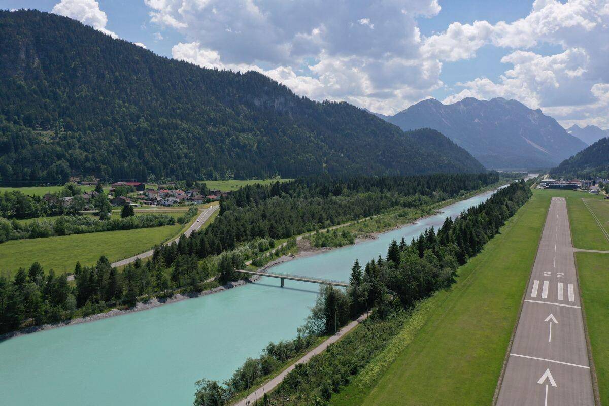 Malerische Flusslandschaft mit Bergen, Wäldern und einem kleinen Flugplatz.