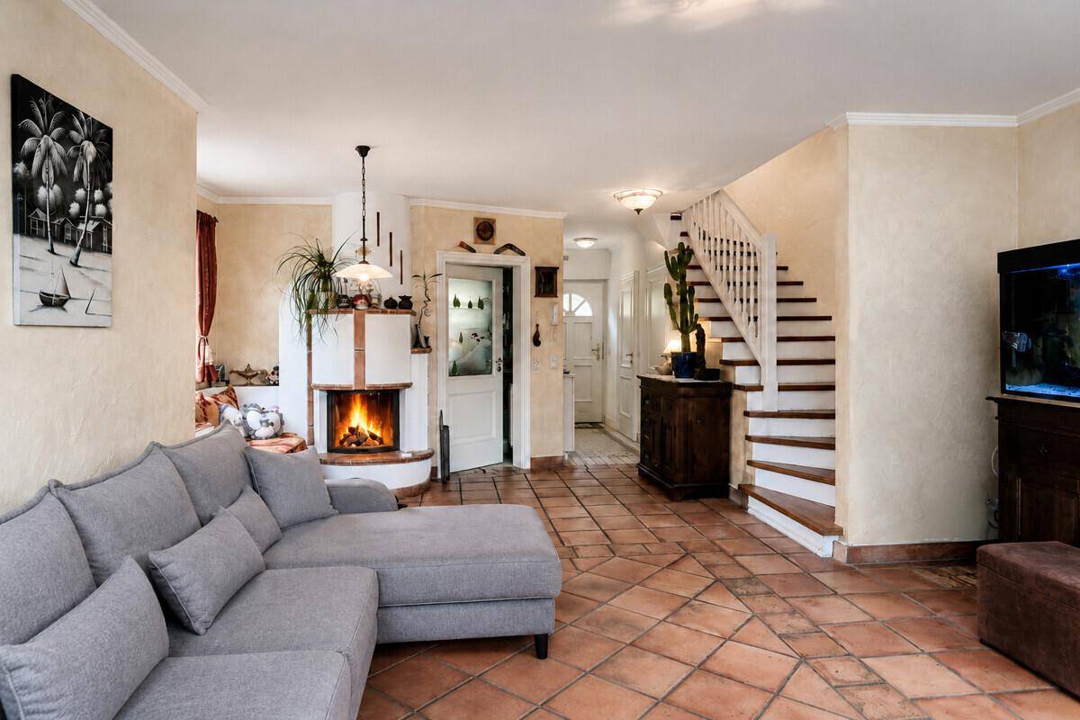 Helles Wohnzimmer mit Kamin, Terrakotta-Fliesenboden und Treppe zum Obergeschoss in traditionellem Stil.