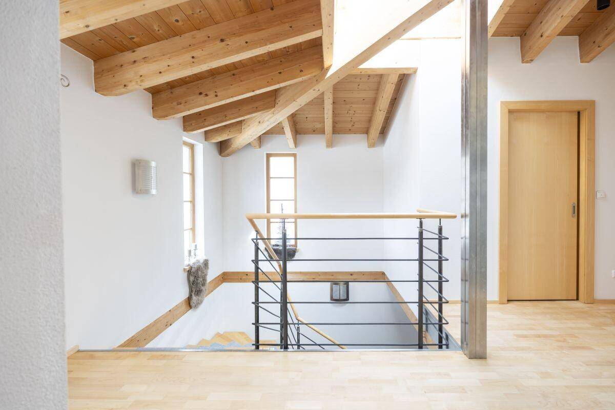 Heller Flur im Obergeschoss mit Holzbalkendecke, Holztreppe und natürlichem Lichteinfall.