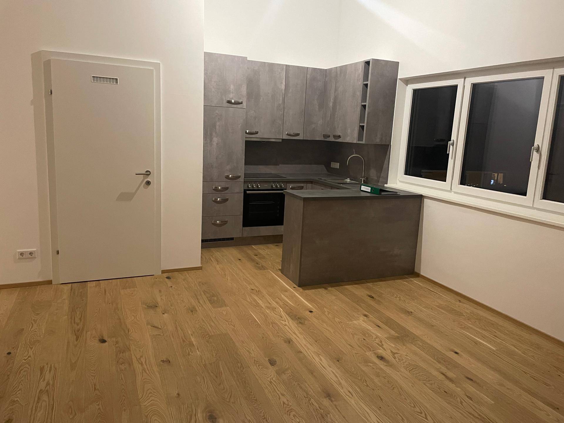 Moderne Einbauküche mit grauen Fronten und Holzboden in einem offenen Wohnbereich.