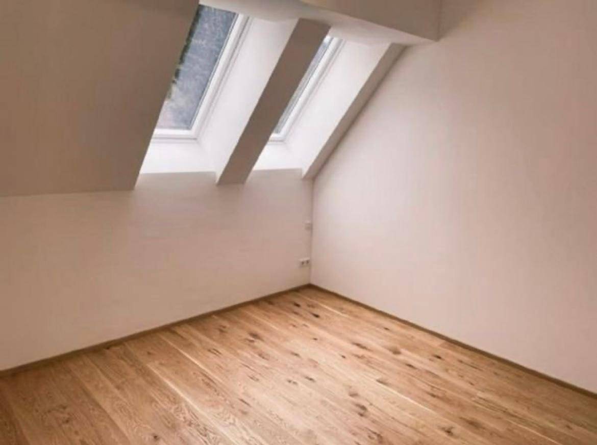 Heller Raum mit Holzboden und zwei Dachfenstern, ideal für ein Schlafzimmer oder Büro.