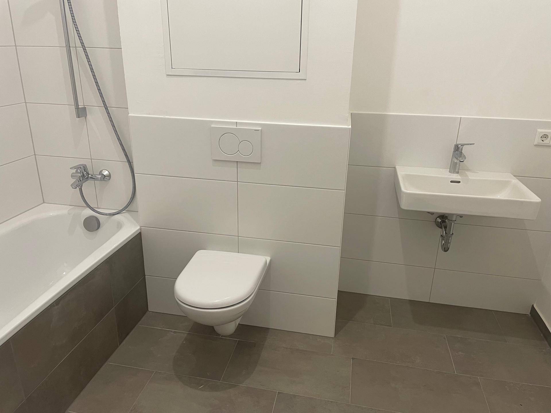Modernes Badezimmer mit Badewanne, wandhängendem WC und Waschbecken in hellen Fliesen.