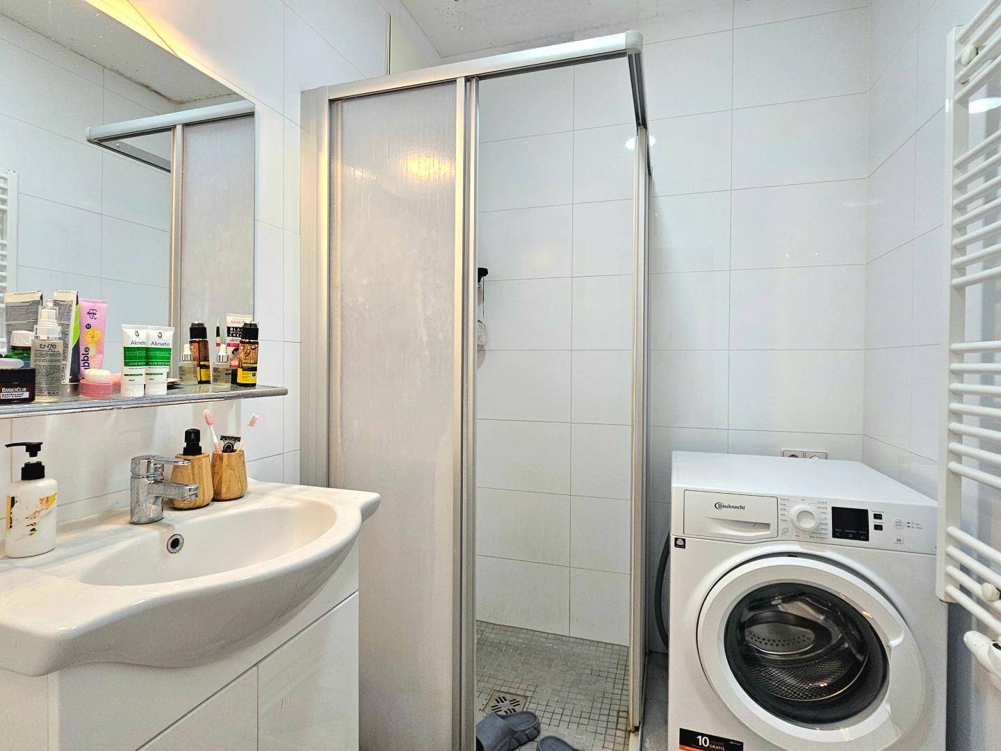Modernes Badezimmer mit Duschkabine, Waschbecken, Waschmaschine und beheiztem Handtuchhalter.
