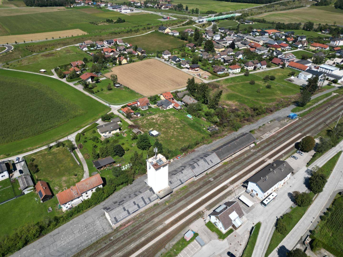 Panoramische Luftaufnahme des Grundstücks mit Bahnhof, angrenzenden Feldern und Wohnsiedlung.