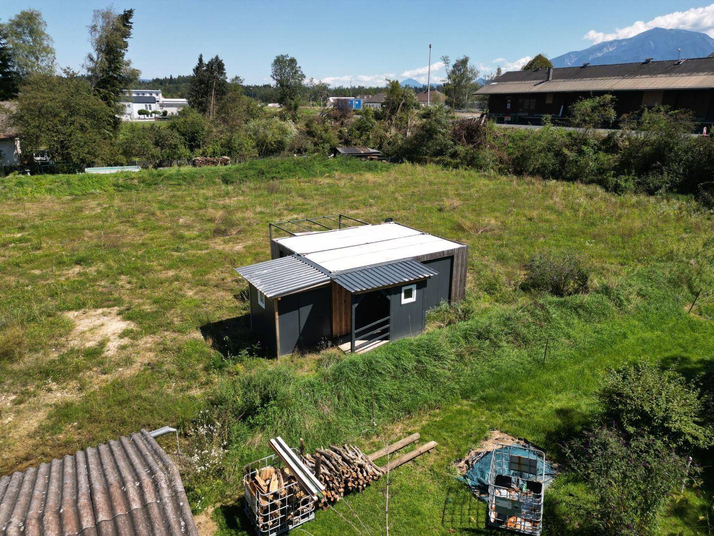 Nahaufnahme der kleinen Hütte auf dem Grundstück mit Holzstapeln und umgebendem Grasland.