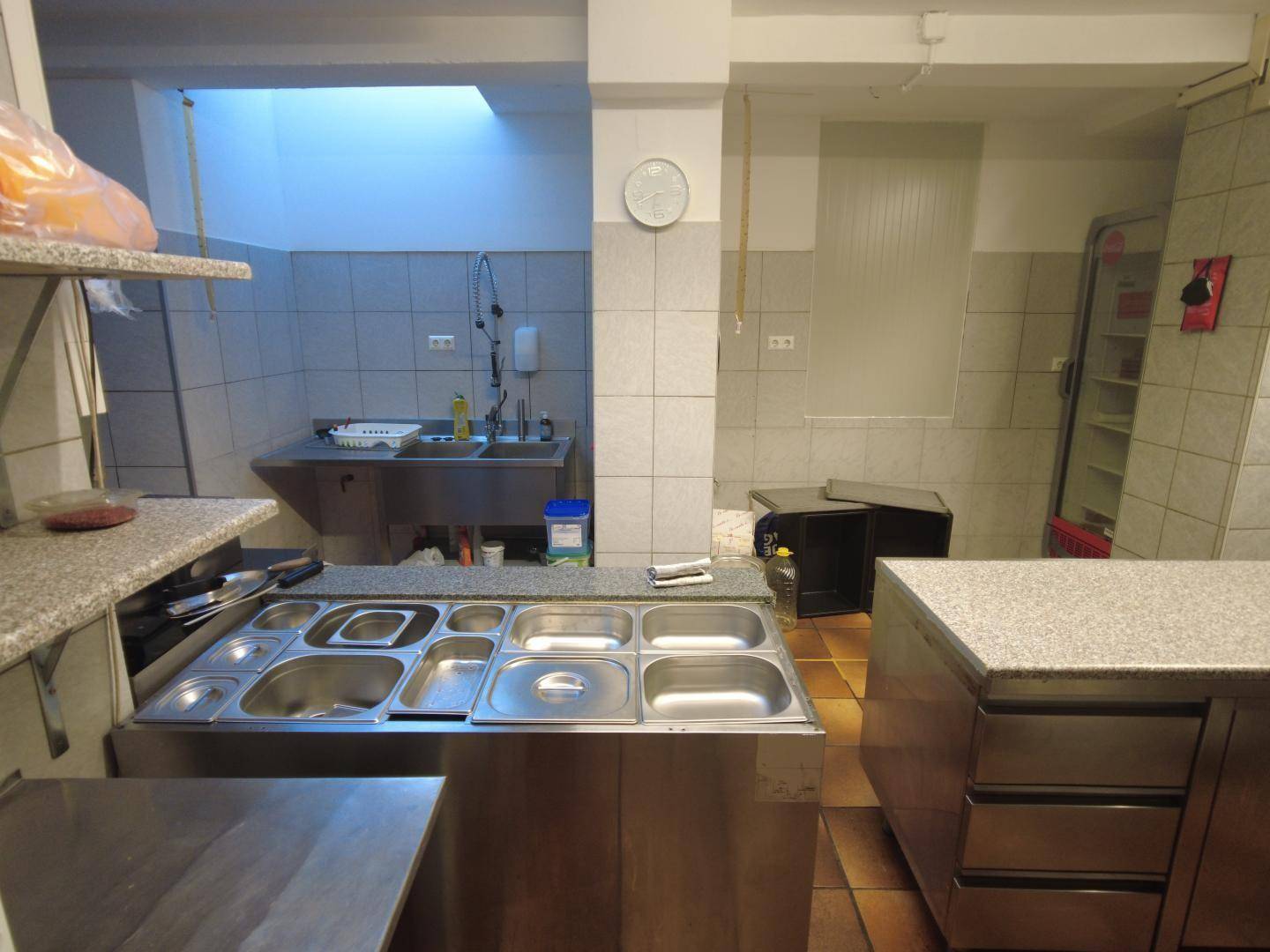 Professionelle Küche mit Edelstahltheke, Warmhaltebecken und gefliesten Wänden.