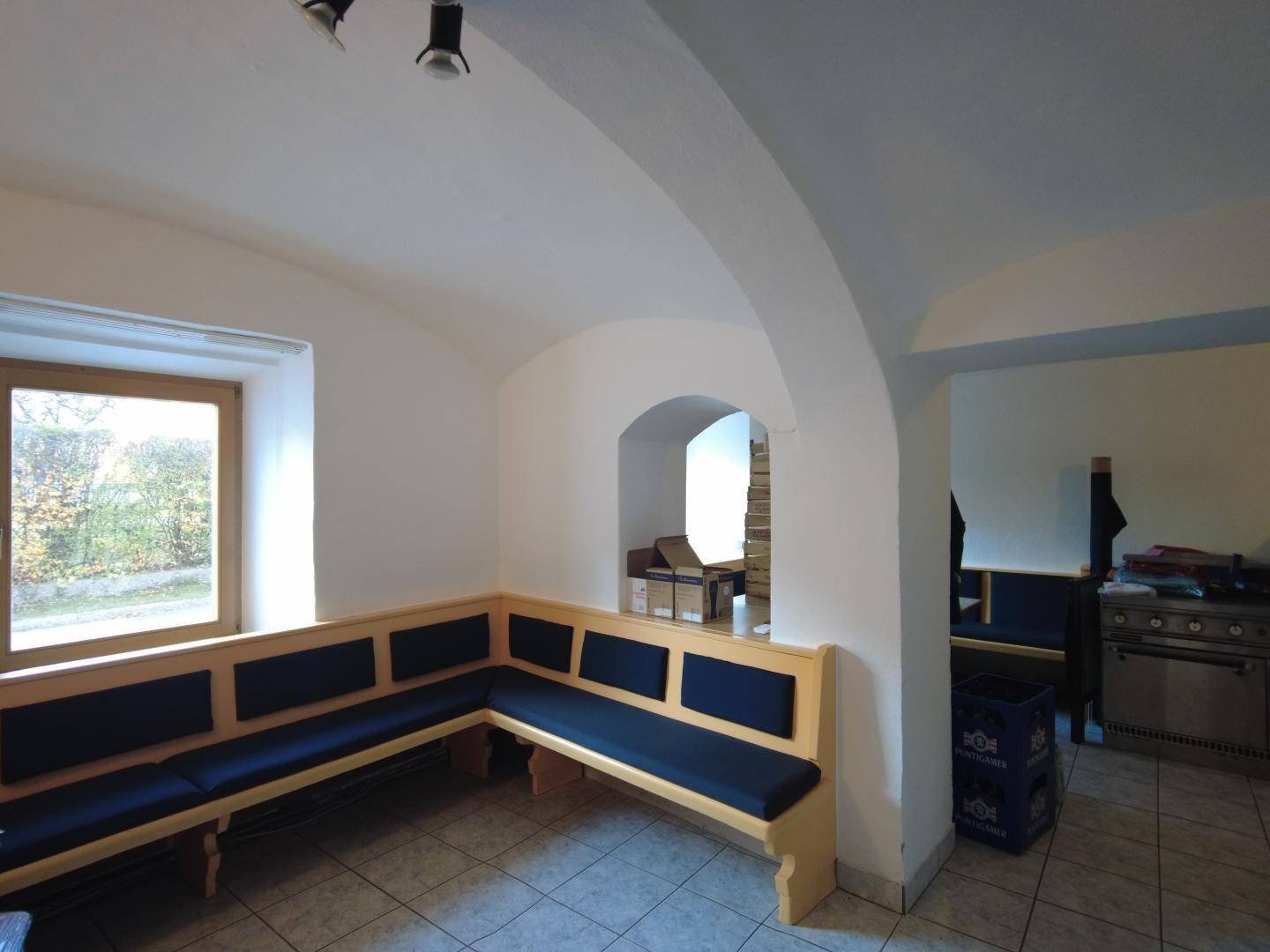 Raum mit Gewölbedecke, Sitzbänken und einem Fenster, das einen Blick ins Grüne bietet.
