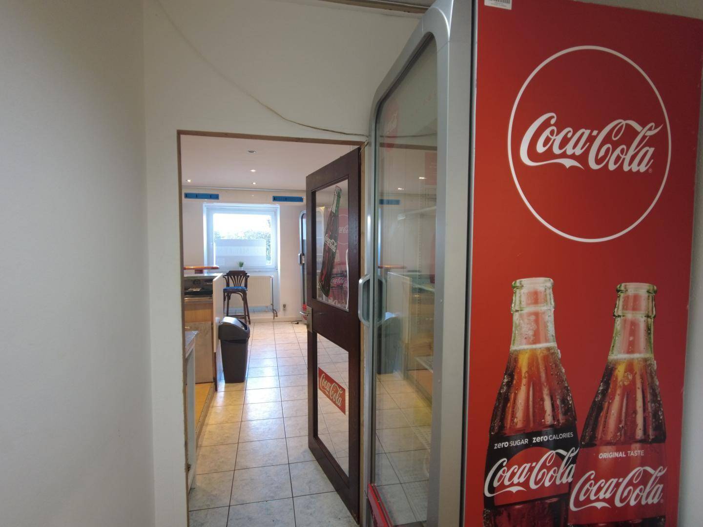 Durchgangsbereich mit Fliesenboden und einer großen Kühlvitrine, die den Blick in den nächsten Raum freigibt.
