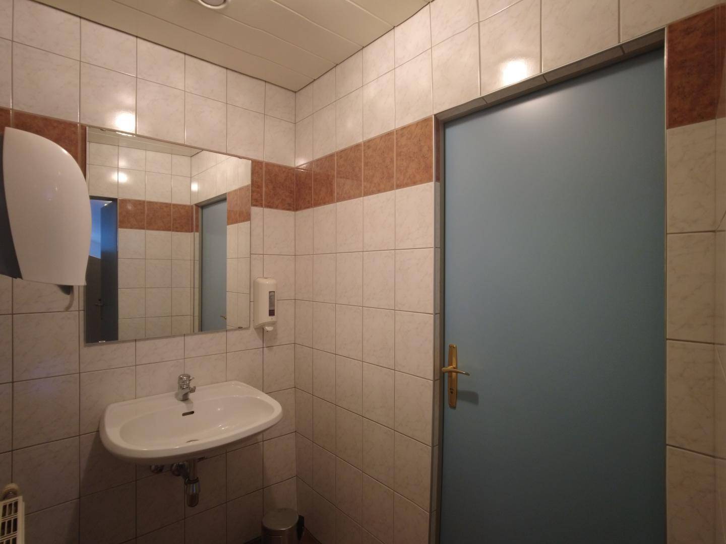 Gefliestes Badezimmer mit Waschbecken, Spiegel und einer blauen Tür.