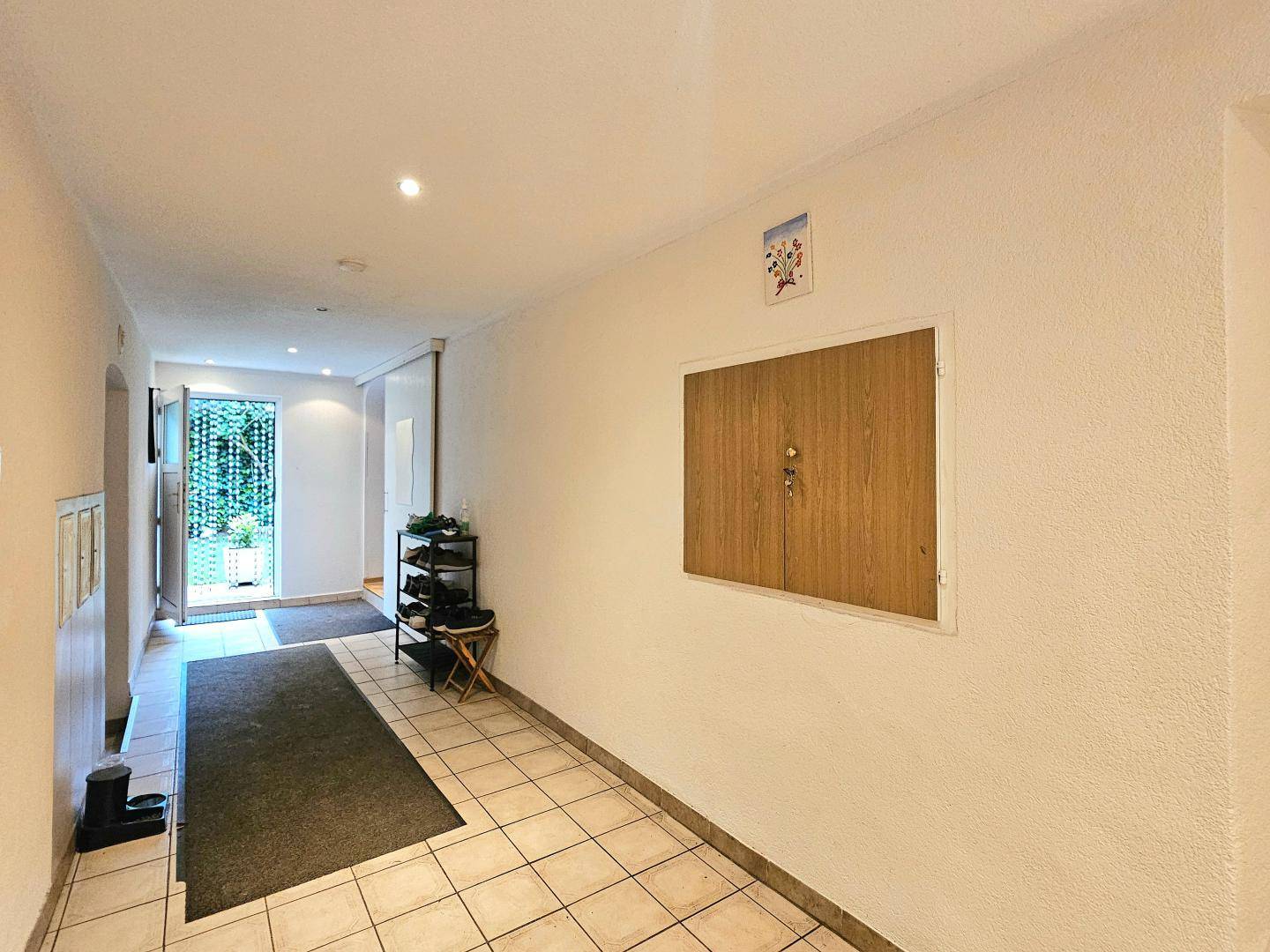 Eingangsbereich mit Fliesenboden, Schuhregal und heller Eingangstür zum Garten.